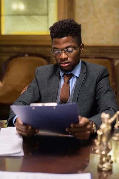Joven abogado exitoso de etnia africana mirando a través de documento jurídico — Foto de Stock