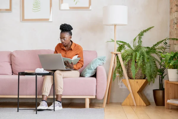 Афроамериканка сидить на дивані і записує нотатки. — стокове фото