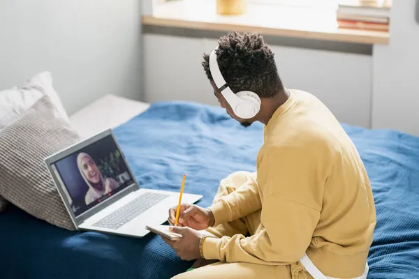 Estudiante contemporáneo de etnia africana sentado en la cama y tomando notas —  Fotos de Stock