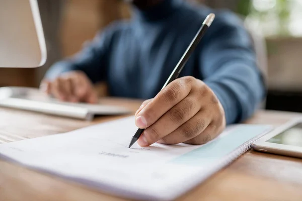 Mão de homem segurando lápis sobre o documento enquanto sentado à mesa — Fotografia de Stock
