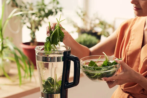Jeune femme au foyer mettre des feuilles d'épinards verts frais dans le mélangeur — Photo