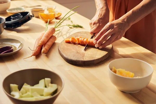 Ruce mladé ženy v domácnosti sekání čerstvé mrkve pro smoothie — Stock fotografie