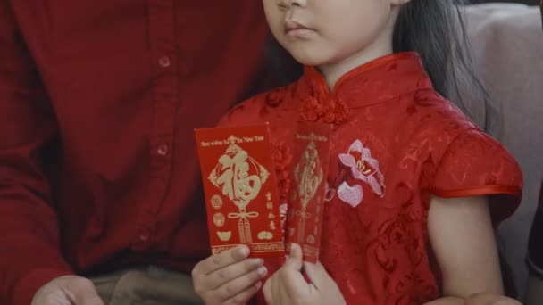 中国の旧正月のはがきを保持する伝統的な唐のスーツで可愛いアジアの5歳の女の子の頬に触れる認識できない父のセクションショット — ストック動画