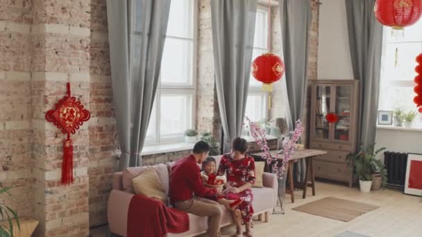 在家里庆祝中国新年的时候 身穿红衫和传统服装的快乐的亚洲父母将礼物篮送给可爱的5岁女儿 手握追踪照片 — 图库视频影像