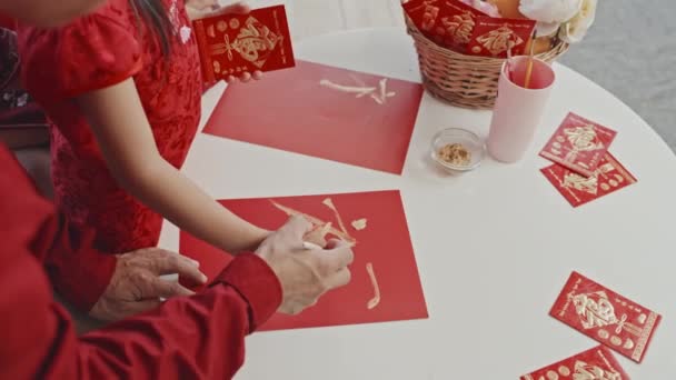 中国の旧正月のためのはがきを作りながら 彼の小さな娘が紙の上に漢字を描くのを助ける認識できないアジアの父親の高角度ショットを開催しました — ストック動画