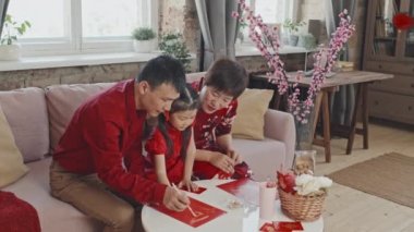 Orta boy Asyalı ebeveynler geleneksel elbiseli 5 yaşındaki tatlı kızlarına Çin Yeni Yıl kartpostalı yaparken yardım ediyorlar.