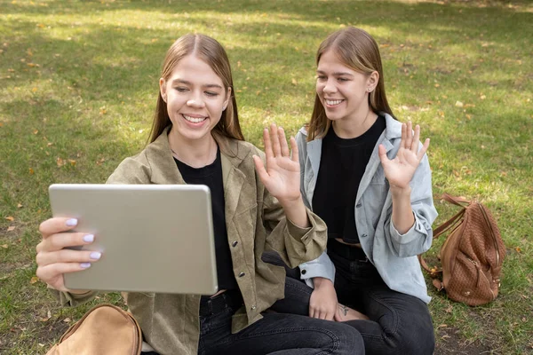Duas meninas alegres acenando as mãos para alguém na tela do tablet — Fotografia de Stock