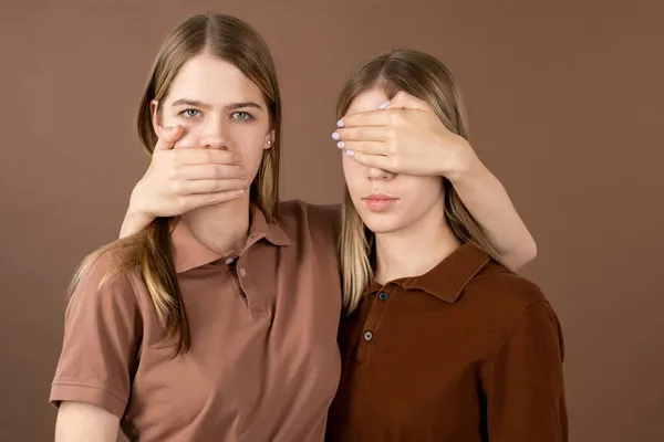 One of twins covering mouth of another girl keeping hand on eyes of her sister — Stock Photo, Image