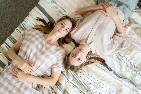 Två unga fridfulla tvillingar i casualwear liggande på sängen — Stockfoto