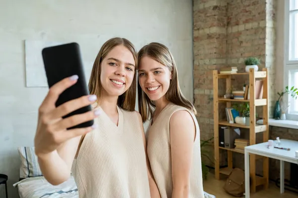 Una delle ragazze gemelle con smartphone fare selfie con sua sorella — Foto Stock