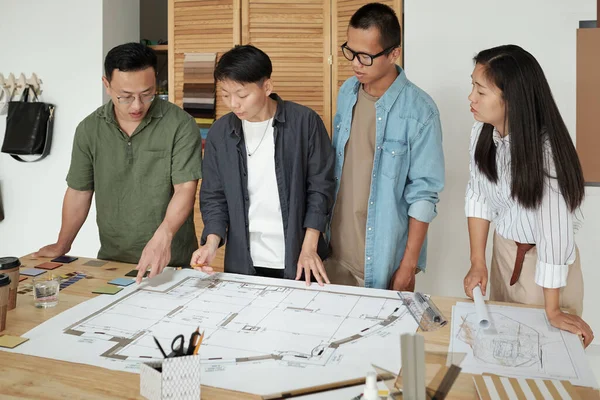 Grupo de jóvenes arquitectos reunidos por mesa con gran boceto — Foto de Stock