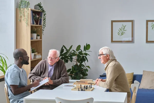 Медсестра розмовляє з літніми чоловіками в будинку престарілих — стокове фото