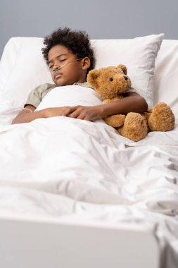 Hasta çocuk oyuncakla hastane yatağında yatıyor.