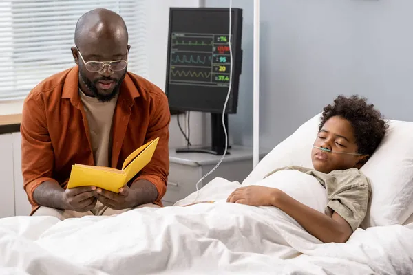 Apa könyvet olvas a fiának a kórházban. — Stock Fotó