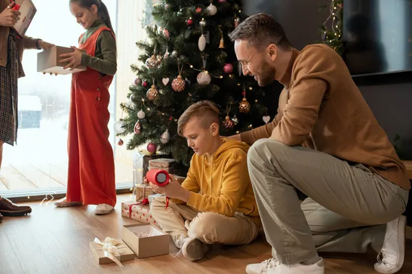 Pai olhando para a reação dos filhos ao presente de Natal — Fotografia de Stock