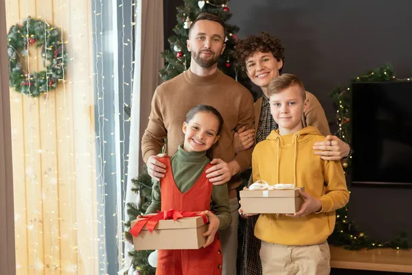 Родители среднего возраста обнимают детей против рождественской елки — стоковое фото