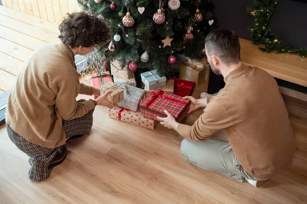 Man en vrouw zetten kerstcadeaus onder boom — Stockfoto