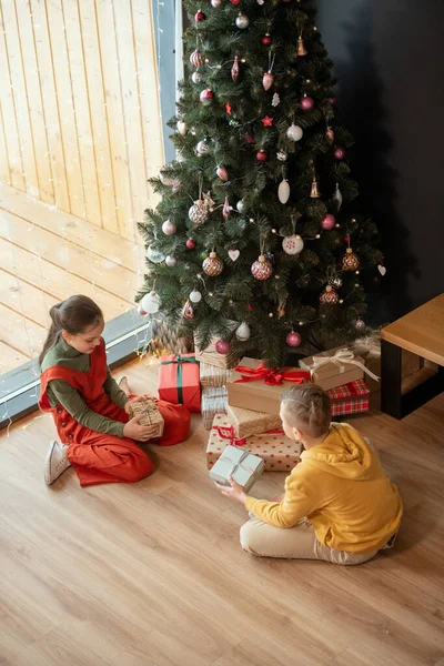 Geschwister sitzen mit Geschenken am Weihnachtsbaum — Stockfoto