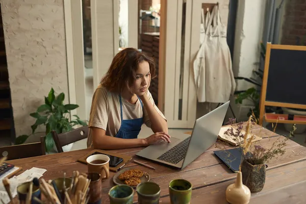 Jonge creatieve vrouw concentreert zich op netwerk tijdens het zitten in workshop — Stockfoto