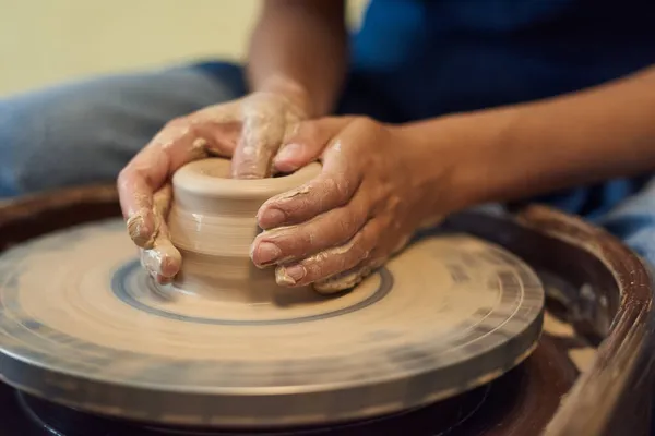 Mãos de jovem artesão segurando por roda de cerâmica rotativa — Fotografia de Stock
