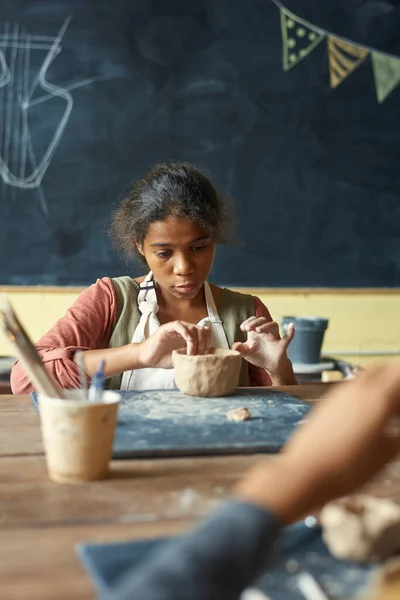 可愛いです若いです女の子でエプロン作る粘土ボウルやマグカップによってテーブル — ストック写真