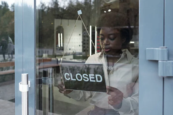 Młody afrykański sklep asystent wisi zamknięty znak na drzwiach butiku — Zdjęcie stockowe