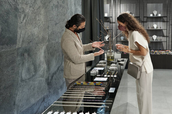 Young male owner of jewelry department consulting female client