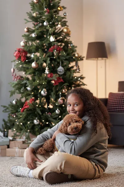 Glückliches Mädchen mit niedlichem Haustier sitzt auf dem Boden gegen den Weihnachtsbaum — Stockfoto