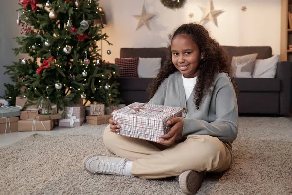 Glückliches süßes afrikanisches Mädchen hält Geschenkbox, während es auf dem Boden sitzt — Stockfoto