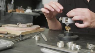 Tanınmayan kadın kuyumcunun orta bölüm PAN 'ı tezgahta oturuyor ve metal yüzükler yapıyor.