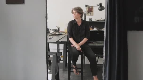 Panポートレートの陽気な女性の宝石商座って椅子に彼女のスタジオと笑顔のためにカメラ — ストック動画