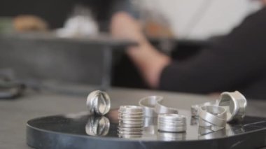 Mücevher stüdyosundaki tepside duran metal halkalardan oluşan PAN 'ı kapat. Arka planda demir testeresi kullanan tanınmayan bir kuyumcu.