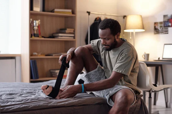 年轻的运动员坐在床上时，用绷带包扎脚 — 图库照片