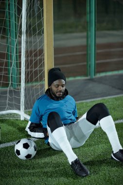 Profesyonel spor üniformalı yorgun futbolcu ağda oturuyor.