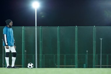 Spor üniformalı genç Afrikalı futbolcu sahada duruyor.