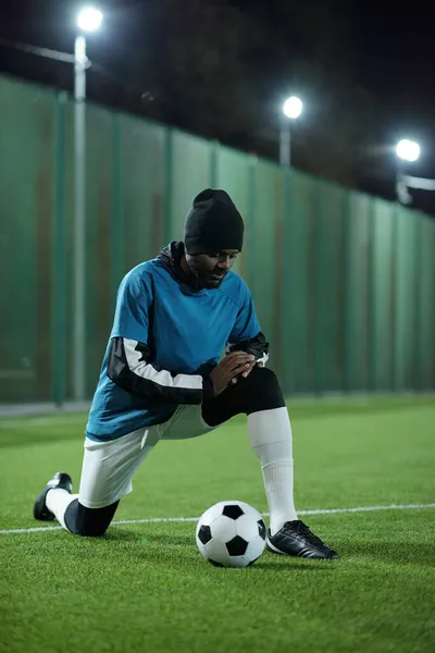 Молодой африканский футболист, стоящий на коленях на футбольном поле — стоковое фото