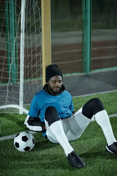 Vermoeide voetballer in professioneel sportuniform zittend aan het net — Stockfoto