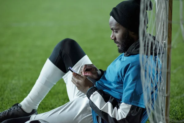 Jogador de futebol sério em mensagens de texto uniformes no telefone móvel — Fotografia de Stock