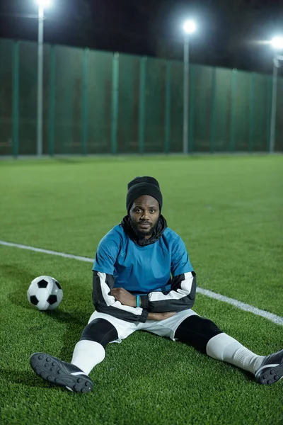 Молодий спокійний чоловік африканської національності сидить на футбольному полі. — стокове фото