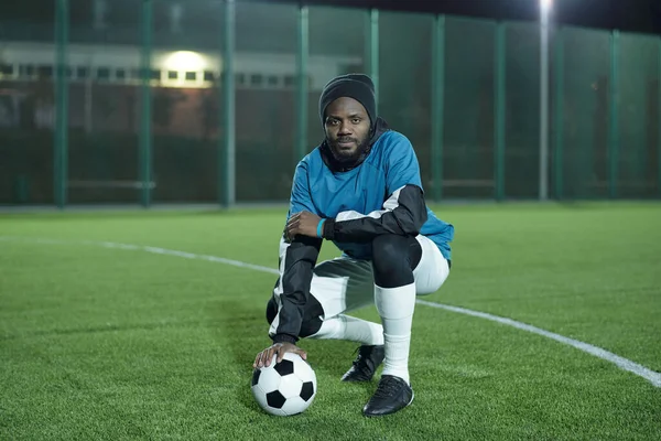 Молодий африканський футболіст з футбольним м'ячем сидить на присілках. — стокове фото