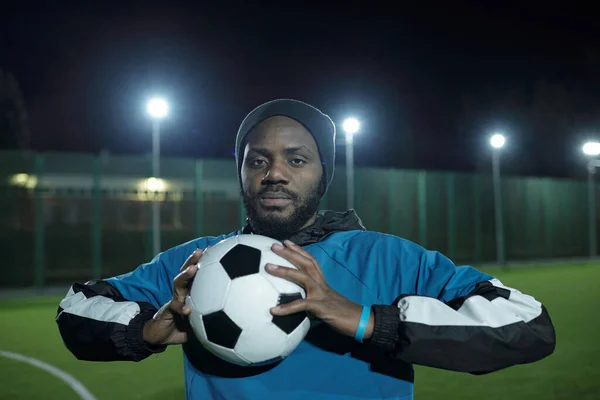 Ung afrikansk man i sportuniform håller fotboll framför sig — Stockfoto