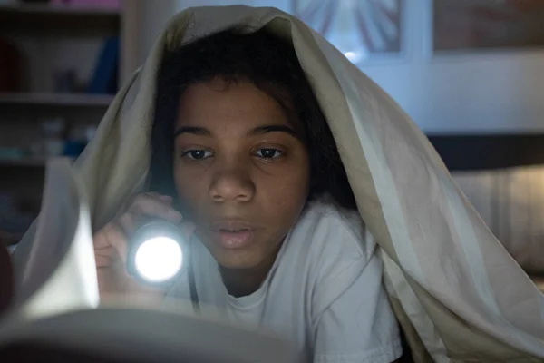 Nieuwsgierig meisje schijnt zaklamp op boek — Stockfoto