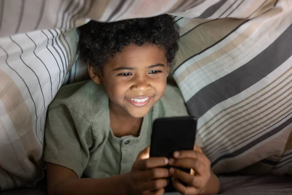 Jongen met moderne telefoon onder dekbed — Stockfoto