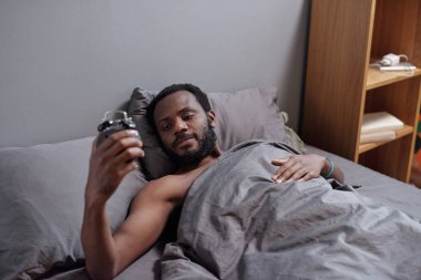 Genç adam uyandıktan sonra elindeki çalar saate bakıyor.