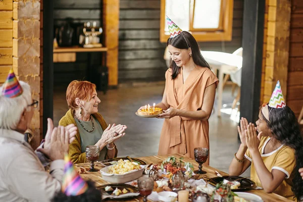 Feliz família batendo palmas enquanto jovem sorrindo mulher carregando bolo de aniversário — Fotografia de Stock