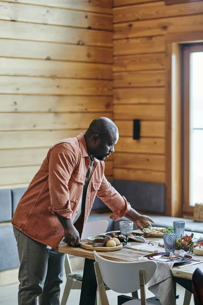 Young African man putting homemade cooked food on festive table — Stock Photo, Image