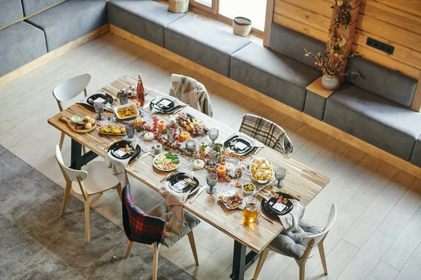 Několik židlí kolem velkého dřevěného jídelního stolu podávané s domácím jídlem — Stock fotografie