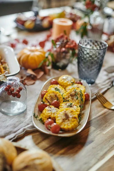 Plate with baked chopped corn and fresh cherry tomatoes standing among kitchenware and decorations — Stock Photo, Image