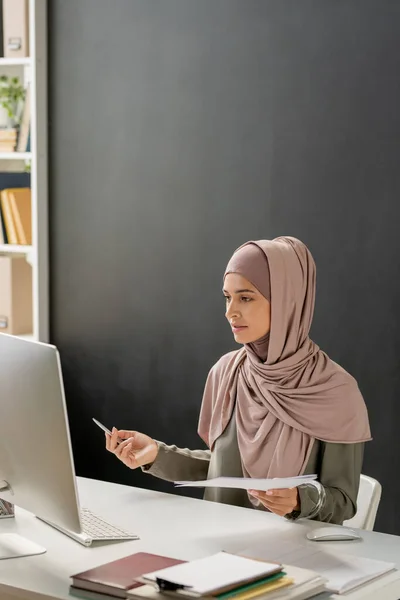 Donna in hijab seduta davanti al computer e che spiega l'argomento della lezione online allo studente — Foto Stock
