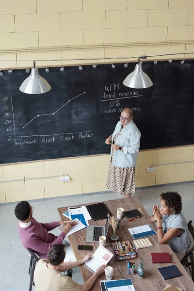 Giovane allenatrice in piedi alla lavagna con grafico e altri dati finanziari — Foto Stock